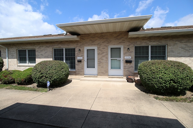 view of exterior entry featuring brick siding and a patio