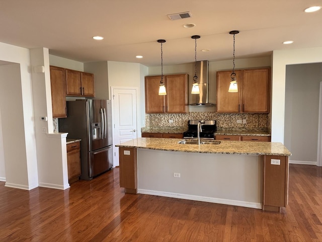 kitchen with wall chimney exhaust hood, dark hardwood / wood-style flooring, stainless steel appliances, and a kitchen island with sink