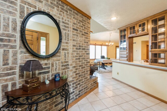 hall with light tile patterned floors, an inviting chandelier, brick wall, and a textured ceiling