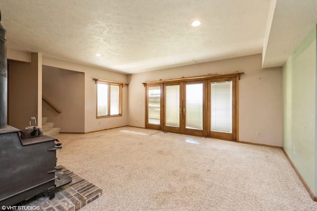 carpeted living room with a textured ceiling, french doors, and a wood stove