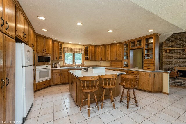 kitchen with brick wall, a kitchen bar, light tile patterned floors, a center island, and white appliances