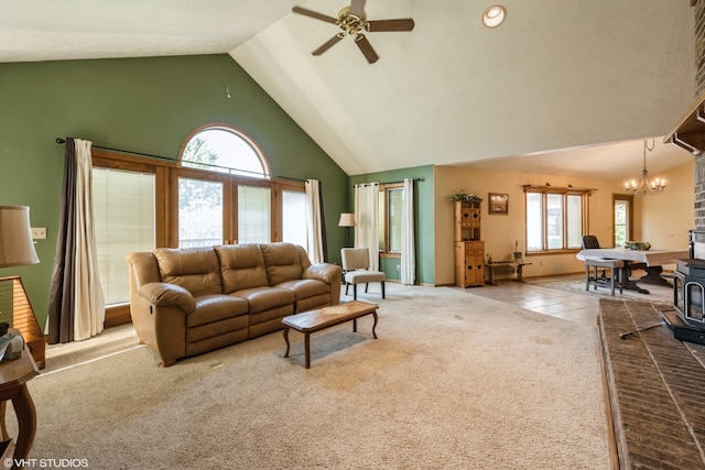 living room featuring ceiling fan with notable chandelier, high vaulted ceiling, a wood stove, and light carpet