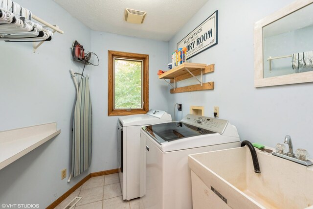 laundry area featuring light tile patterned floors, sink, separate washer and dryer, and a textured ceiling