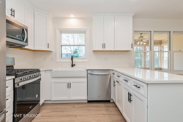 kitchen featuring white cabinets, sink, light hardwood / wood-style floors, kitchen peninsula, and stainless steel appliances