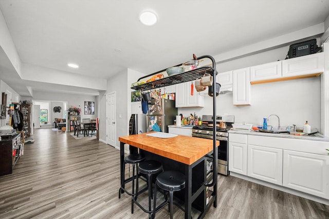 kitchen with stainless steel appliances, wood counters, light hardwood / wood-style flooring, a breakfast bar area, and white cabinets