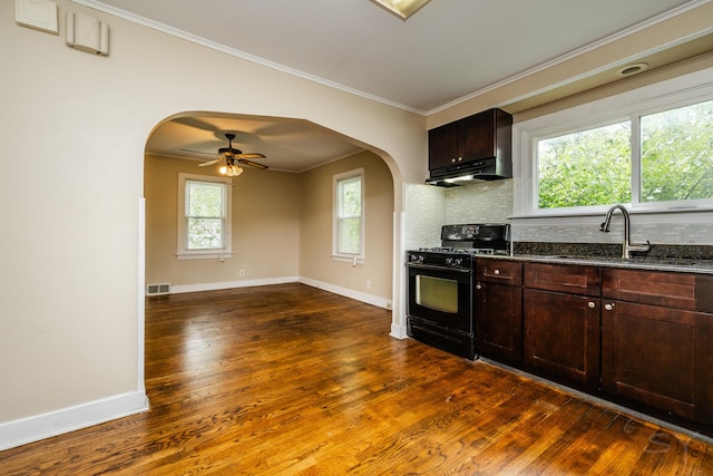 kitchen featuring arched walkways, a sink, black gas stove, decorative backsplash, and crown molding