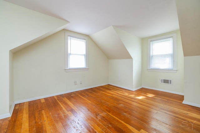 bonus room featuring lofted ceiling, visible vents, baseboards, and wood finished floors