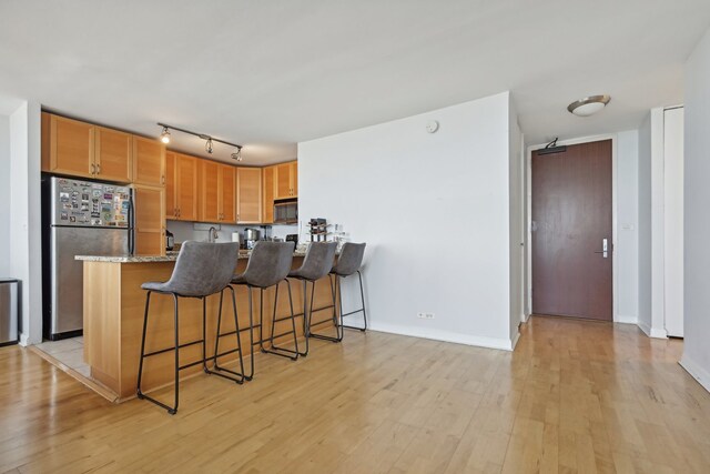 kitchen with light hardwood / wood-style floors, stainless steel refrigerator, track lighting, and light stone countertops