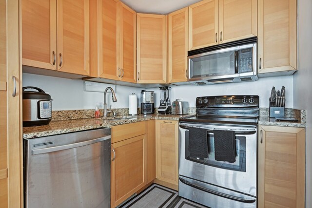 kitchen with appliances with stainless steel finishes, sink, stone counters, and light brown cabinets