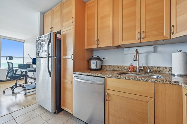 kitchen featuring stainless steel appliances, sink, light tile patterned floors, dark stone counters, and light brown cabinetry