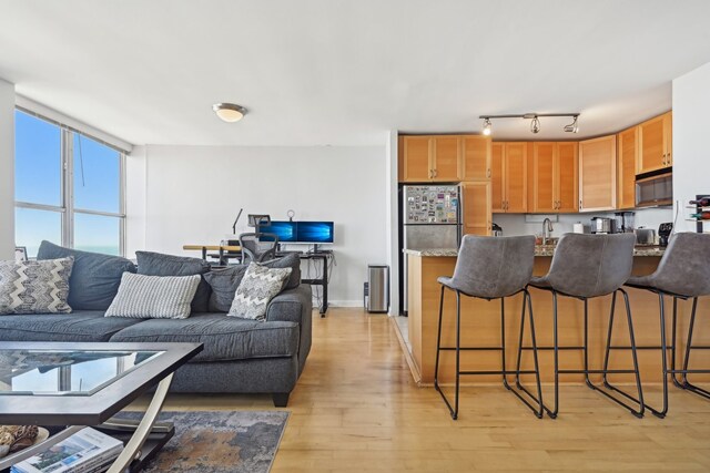 kitchen with light hardwood / wood-style flooring, a kitchen bar, sink, track lighting, and stainless steel fridge