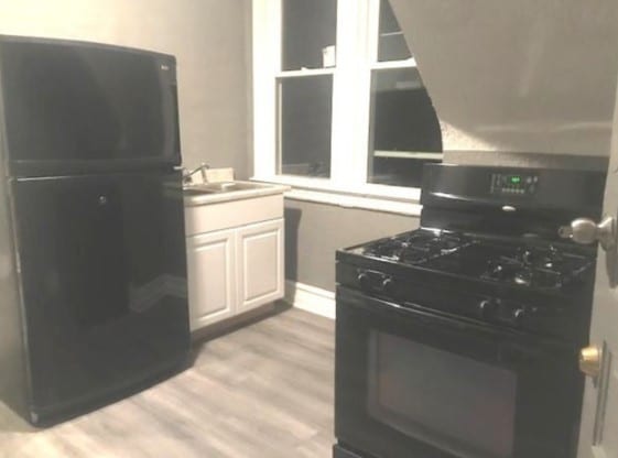 kitchen with sink, black appliances, white cabinetry, and light hardwood / wood-style flooring