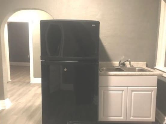 interior space featuring sink, white cabinetry, black fridge, and light hardwood / wood-style floors