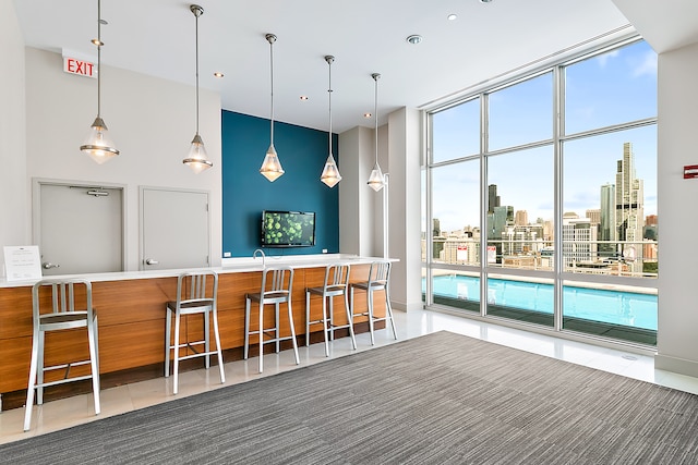 kitchen with a breakfast bar, kitchen peninsula, tile patterned flooring, hanging light fixtures, and a wall of windows