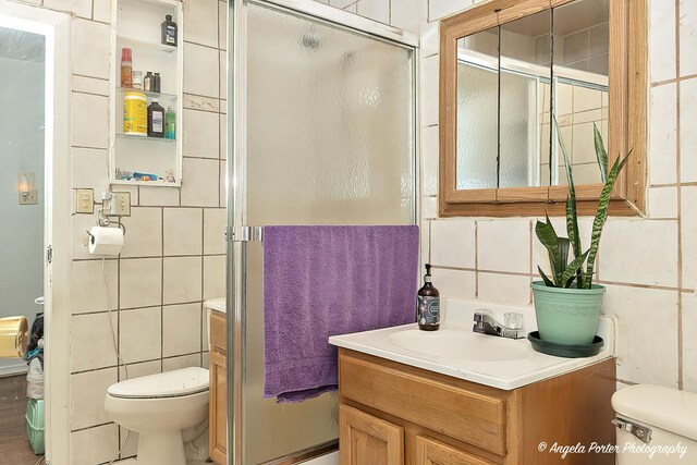 bathroom featuring tile walls, toilet, vanity, and walk in shower