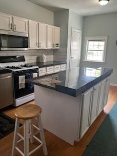 kitchen featuring wood finished floors, white range with gas cooktop, a center island, stainless steel microwave, and dark countertops