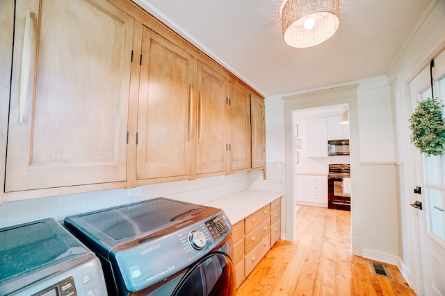 clothes washing area featuring light wood-type flooring, cabinets, washing machine and dryer, and ornamental molding