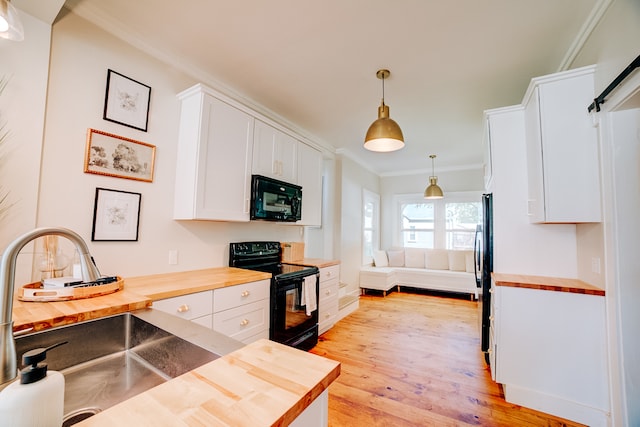 kitchen with wood counters, ornamental molding, white cabinets, light hardwood / wood-style floors, and black appliances