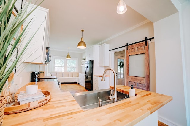 kitchen featuring a barn door, decorative light fixtures, stainless steel appliances, white cabinetry, and a sink