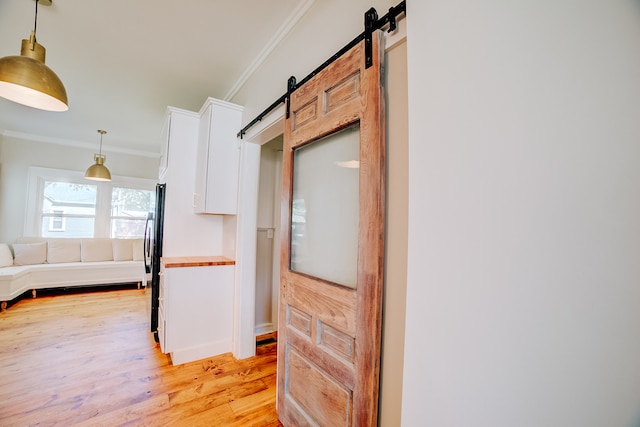 kitchen with decorative light fixtures, light hardwood / wood-style floors, crown molding, black fridge, and a barn door