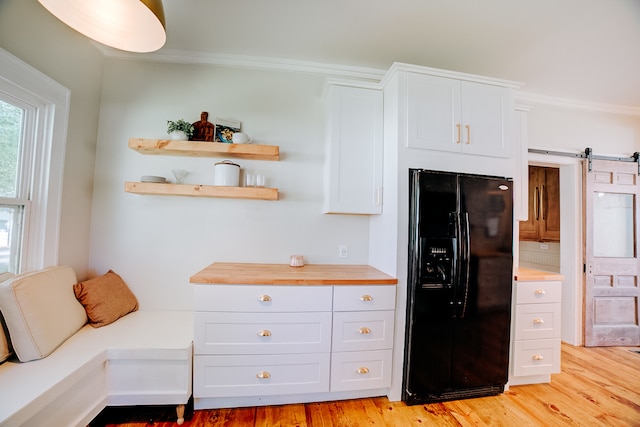 kitchen with white cabinets, light wood-type flooring, a barn door, and black fridge with ice dispenser