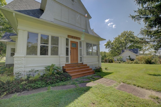 view of front of property with entry steps, a shingled roof, and a front lawn