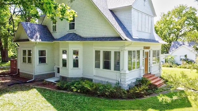 back of property featuring entry steps, a yard, a shingled roof, and a sunroom