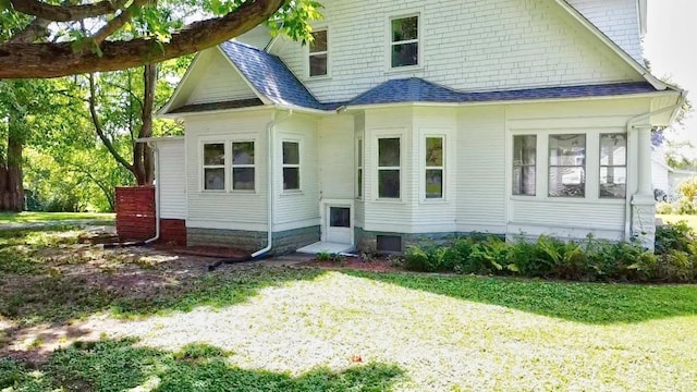 back of house with a shingled roof, entry steps, and a yard