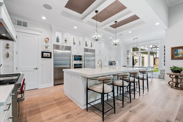 kitchen with an inviting chandelier, light hardwood / wood-style flooring, high quality appliances, a large island with sink, and hanging light fixtures