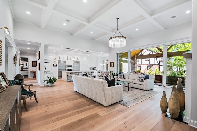 living room with light hardwood / wood-style flooring, a notable chandelier, beam ceiling, and coffered ceiling