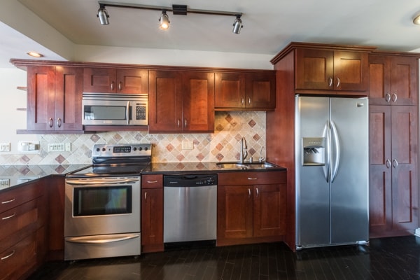 kitchen with dark stone countertops, rail lighting, stainless steel appliances, sink, and decorative backsplash