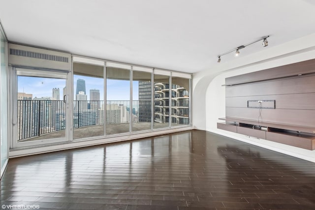 interior space featuring a city view, a wall of windows, rail lighting, and wood finished floors