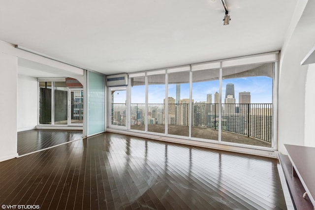 spare room featuring a city view, track lighting, wood finished floors, a wall of windows, and baseboards