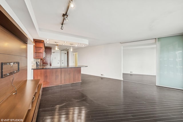 interior space featuring dark wood-type flooring, open shelves, a sink, dark countertops, and a peninsula