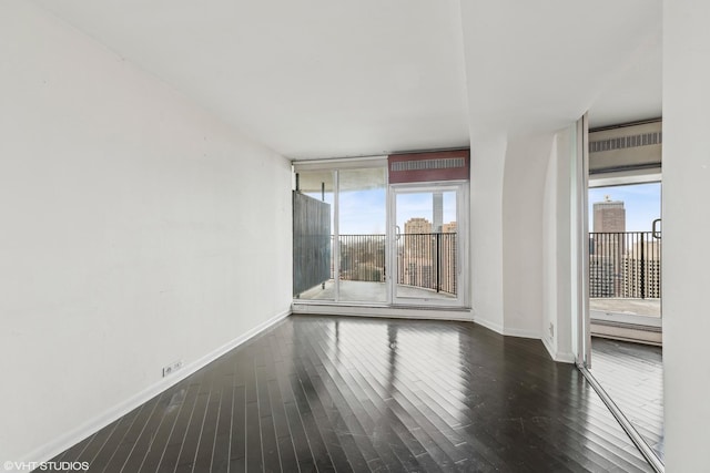 empty room featuring a wealth of natural light, a wall of windows, baseboards, and wood finished floors