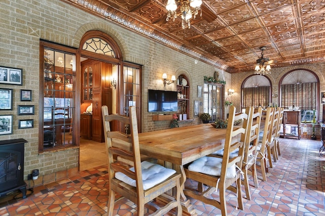 dining room featuring ceiling fan, an ornate ceiling, brick wall, tile patterned floors, and a wood stove