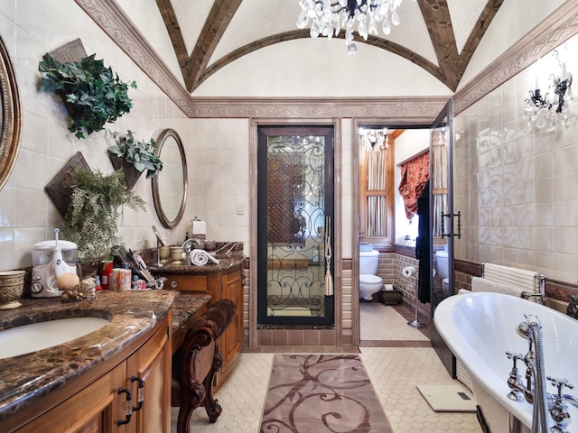 full bathroom featuring tile walls, a freestanding bath, vaulted ceiling, vanity, and a chandelier