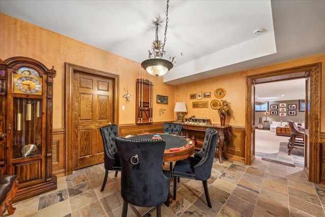 dining area with a wainscoted wall and stone tile floors