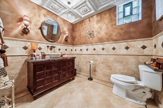 bathroom featuring tile patterned flooring, toilet, vanity, tile walls, and wainscoting