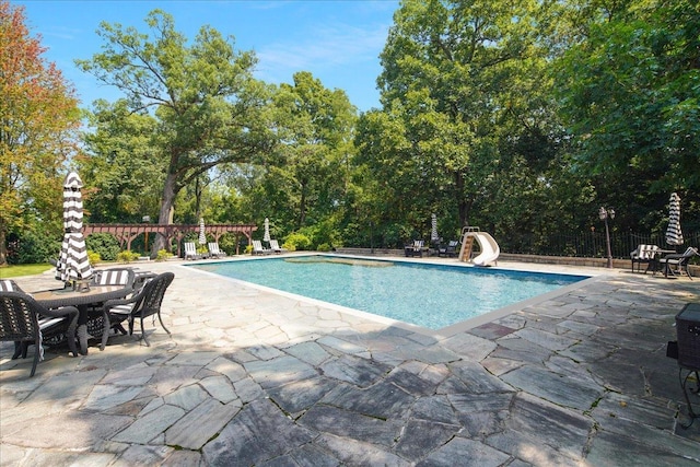 view of pool featuring a fenced in pool, fence, a water slide, and a patio