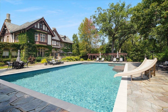 outdoor pool with a patio area, a pergola, and a water slide