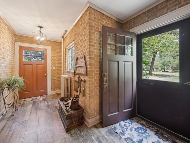 foyer featuring a healthy amount of sunlight, a notable chandelier, brick wall, and wood finished floors