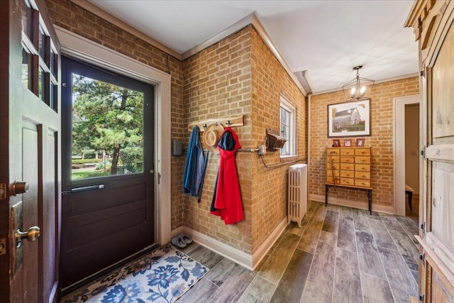 doorway with baseboards, brick wall, radiator heating unit, wood finished floors, and an inviting chandelier