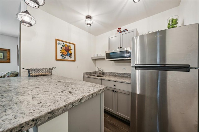 kitchen featuring gray cabinetry, a sink, appliances with stainless steel finishes, light stone countertops, and dark wood finished floors