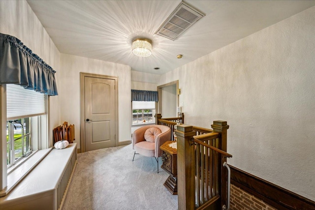 living area featuring a textured wall, visible vents, carpet flooring, and an upstairs landing