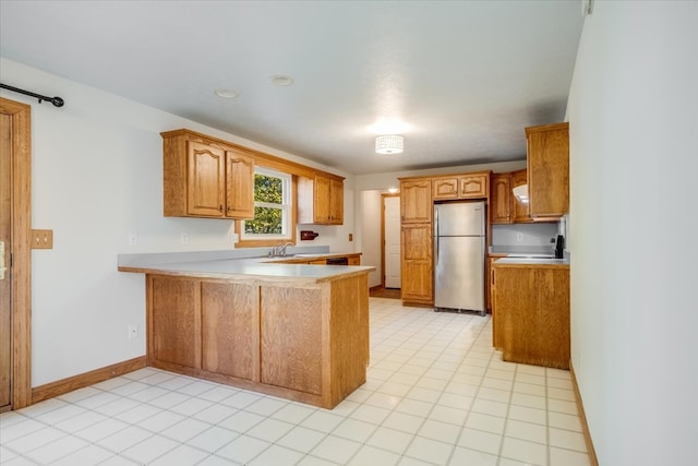 kitchen with stainless steel fridge, kitchen peninsula, sink, and light tile patterned flooring