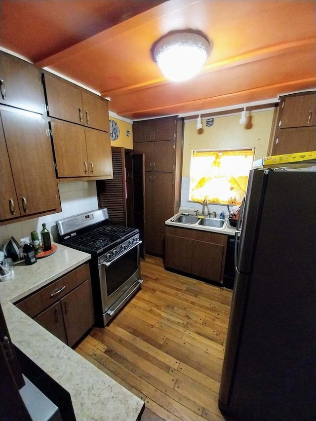 kitchen with black fridge, light wood-type flooring, stainless steel range with gas stovetop, and sink