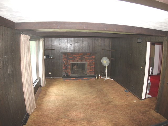 living room with beamed ceiling, wood walls, a brick fireplace, and carpet flooring