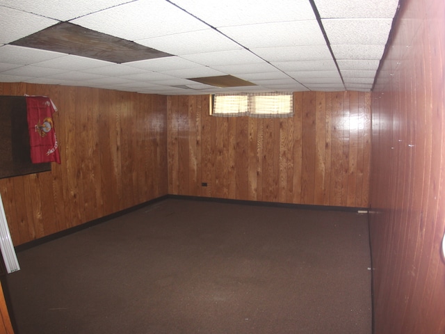 basement featuring wood walls, a paneled ceiling, and carpet flooring