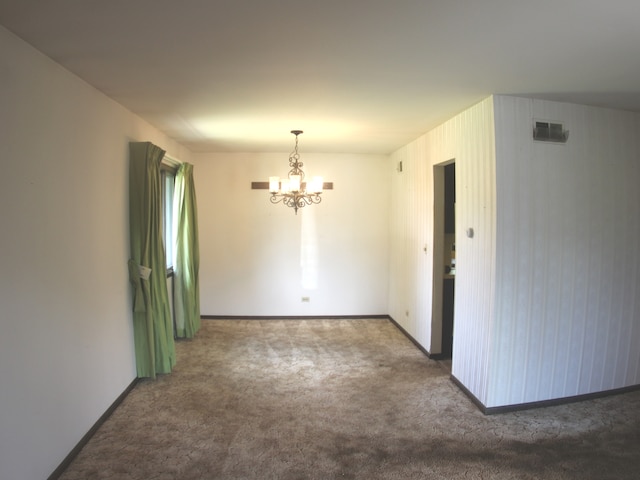 carpeted empty room with an inviting chandelier